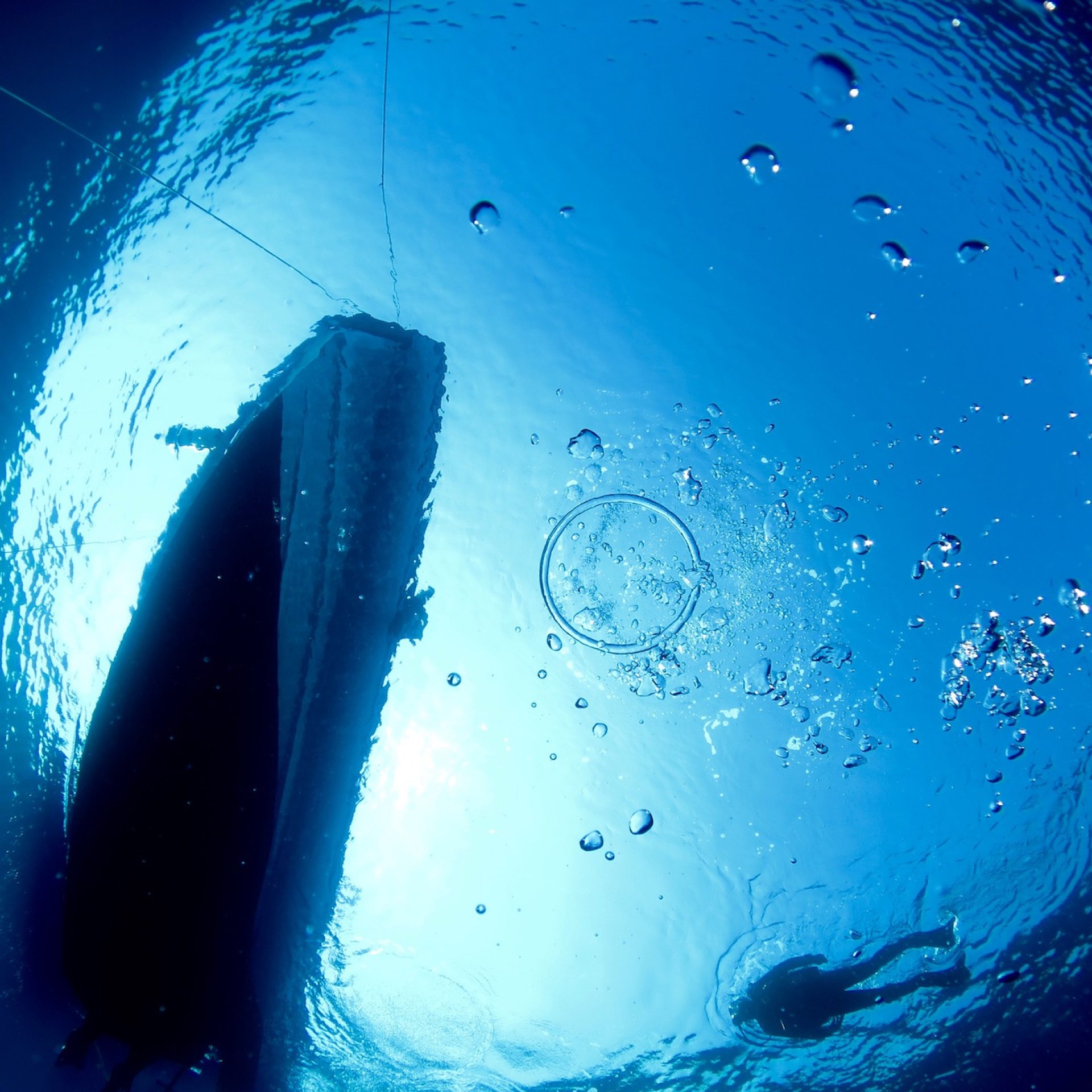 Vista subacquea dal basso della barca in superficie con sub in risalita e bolle d’aria