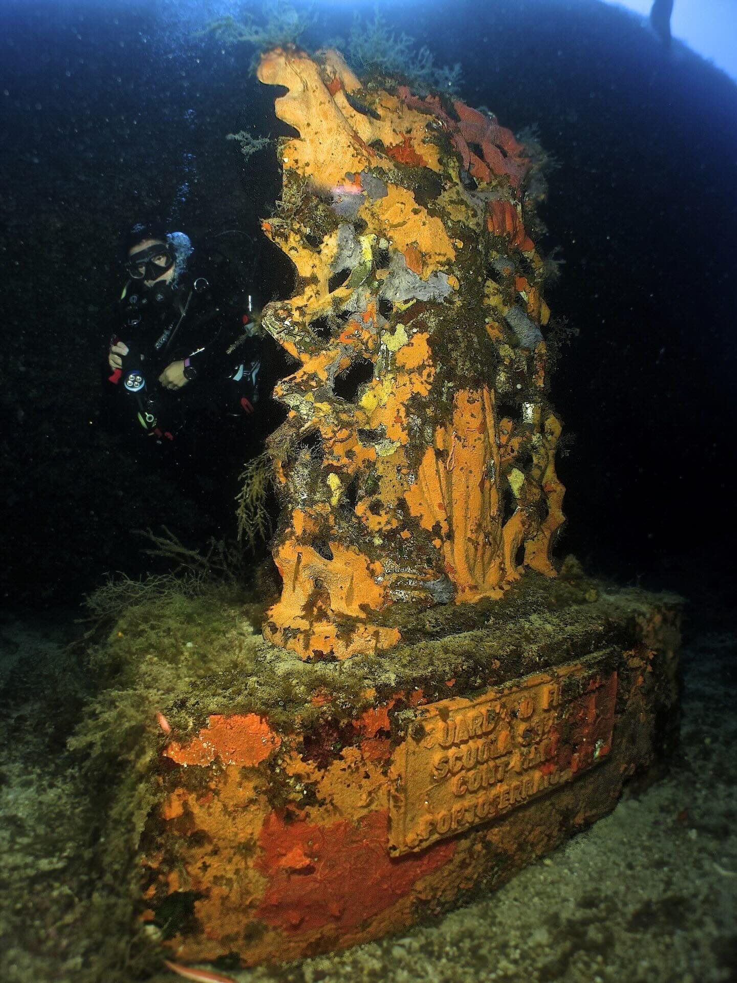 Subacqueo accanto alla statua sommersa del Cristo, ricoperta di spugne
